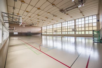 The inside of the Old sports hall. One side is notably covered with windows. The floor is beige and has many lines.