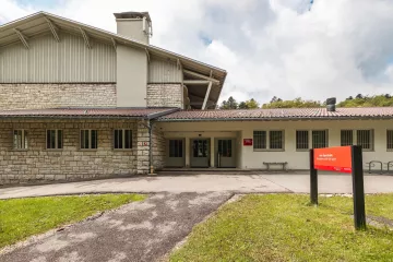 The Old sports hall from the outside. We see the building bain entry and a sign with the name of the building in French “Ancienne salle de sport” and German “Alte Sporthalle”